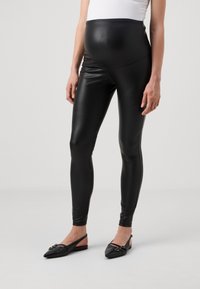 Leggings en simili cuir noir avec une taille haute, un design ajusté et une texture lisse et brillante. Associés à des chaussures à talons plats noires.