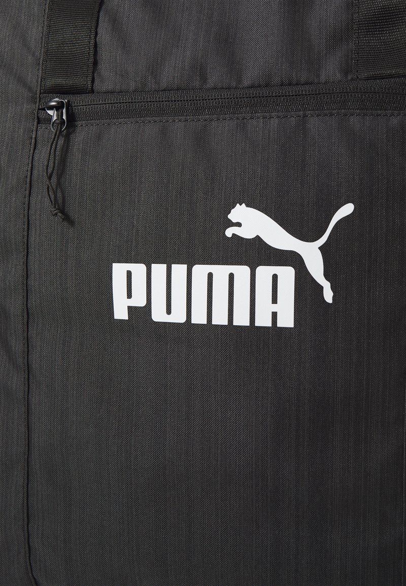 Borsa in tessuto nero con logo Puma bianco. Ha una tasca con zip e una superficie testurizzata, progettata per resistenza e funzionalità.