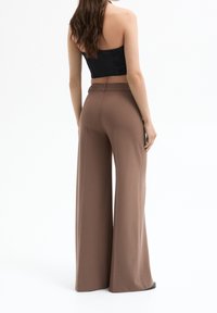 Hnědé široké kalhoty vyrobené z měkké tkaniny s vysokým pasem, s hladkou texturou a minimalistickým designem, stylizované s černým crop topem.