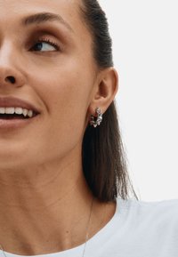 Strieborné geometrické náušnice s hrotmi a jedinečným tvarom, ktoré nosí osoba s dlhými vlasmi. Pozadie je jednoduché biele, čo zdôrazňuje náušnice.