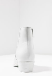Botín de cuero blanco hasta el tobillo con puntera redondeada, cremallera lateral y tacón bajo apilado. Textura suave y diseño minimalista.