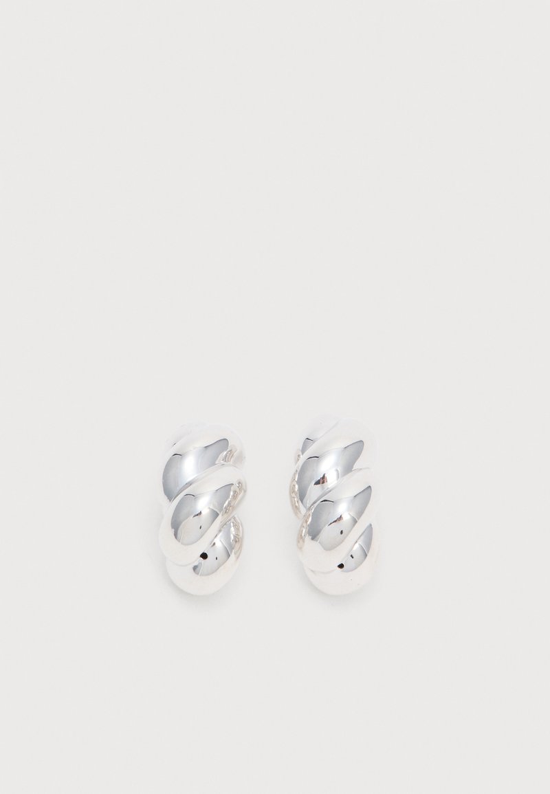 Paire de boucles d’oreilles en forme d’anneaux torsadés ton argent brillant sur fond blanc.