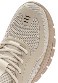 Bottines de sport beige en matériaux en mesh et synthétiques, avec une tige texturée, un système de laçage et une semelle en caoutchouc épaisse.
