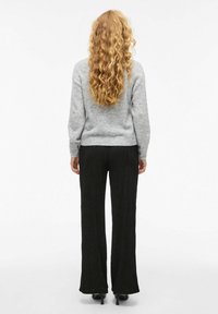 Un pull en maille gris associé à un pantalon large noir ; les deux ont une finition texturée. La silhouette est décontractée, avec des poignets ajustés.