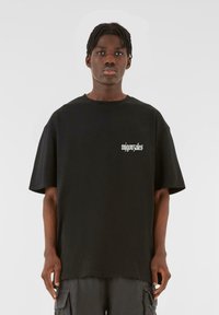 Black oversized t-shirt made of cotton, featuring a round neckline and short sleeves. "mijonzales" printed in white on the chest.