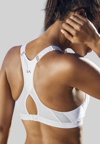 Sostenitore sportivo bianco con dettagli in rete, design a schiena incrociata, spalline regolabili e branding discreto. Tessuto morbido con una leggera lucentezza.