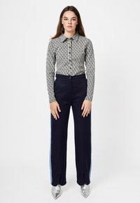 Long-sleeve collared shirt with a geometric pattern in cream and navy, paired with navy trousers featuring light blue side stripes and silver pointed shoes.