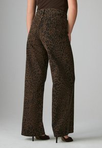 Leopardmönstrade vida byxor i texturerat tyg med ett brunt och svart mönster, med traditionella bakfickor och hög midja.