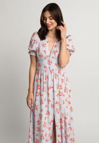 Jasnoniebieska sukienka maxi w kwiaty z bufiastymi rękawami, głębokim dekoltem w kształcie litery V i guzikami w talii. Ma różowe wzory róż i rozcięcie po bokach.