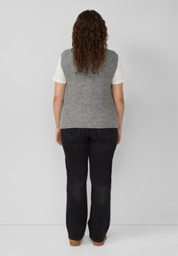 Grijze gebreide mouwloze vest met een gestructureerd patroon, gedragen over een wit T-shirt, gecombineerd met zwarte flared jeans en een paar bruine schoenen. Achteraanzicht.