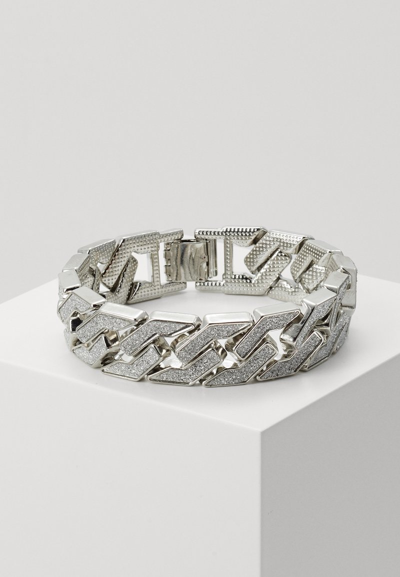 Bracelet à maillons en argent avec surfaces texturées et scintillantes exposé sur un piédestal blanc sur fond uni.