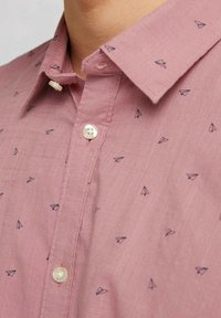 Camicia rosa con bottoni e un motivo delicato di aeroplani di carta in blu navy. Tessuto liscio, con colletto classico e bottoni dall'aspetto perlato.