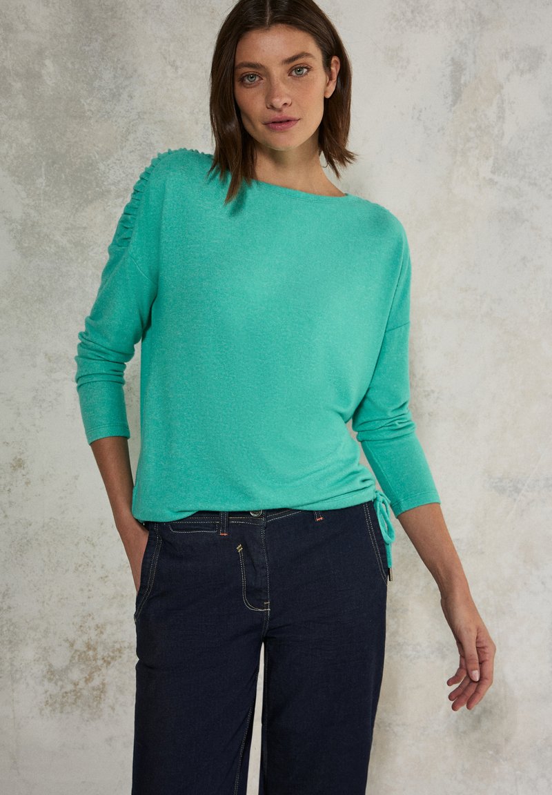 Maglione turchese a maniche lunghe con dettagli texturizzati sulle spalle, vestibilità rilassata, scollatura rotonda, abbinato a jeans blu scuro.