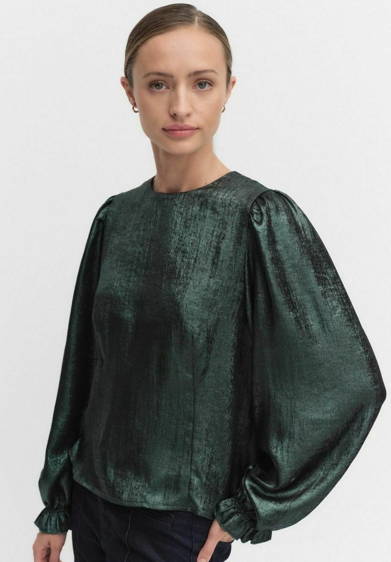 Ciemnozielona satynowa bluzka o błyszczącej teksturze, z balonowymi rękawami i marszczonymi mankietami. Posiada okrągły dekolt oraz gładkie wykończenie.