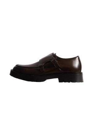 Mocassin en cuir marron foncé à double bride, doté d’une épaisse semelle noire crantée, présenté de profil sur fond blanc.