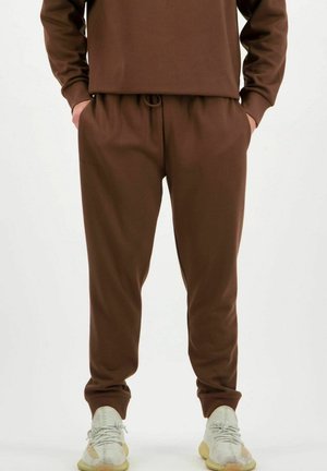 Brauner Hoodie und passende Sweatpants aus einem weichen, strukturierten Stoff. Die Hose hat einen elastischen Bund und einen elastischen Saum. Helle Sneakers.