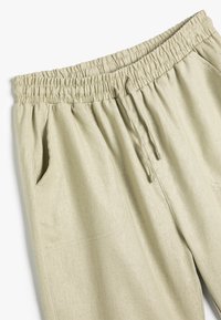 Lys beige trækbåndbukser lavet af blødt stof med elastisk talje og to sidelommer. Dertil kommer en afslappet pasform og enkelt design.