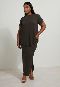 Braunes, strukturiertes Zweiteiler-Outfit mit einer lockeren Bluse und einem langen Rock mit seitlichem Schlitz. Getragen mit strappy, metallischen Sandalen.