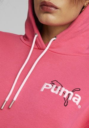 Sudadera rosa con un bolsillo canguro frontal, cordones blancos y logo bordado en blanco y negro de Puma en el pecho. Textura del tejido suave.