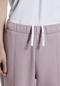 Hellviolette Jogginghose mit strukturierter Stoffqualität, elastischem Bund und weißem Kordelzug. Mit seitlichen Naht-Details.