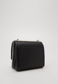 Černá kožená kabelka přes rameno se stříbrným řetízkovým popruhem a vystouplým logem "Calvin Klein Jeans" na zadní kapse.