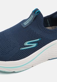 Adidași slip-on de culoare albastru marin cu textură tricotată, având o talpă albă și accente teal, inclusiv un logo și o bandă pentru a facilita îmbrăcarea.