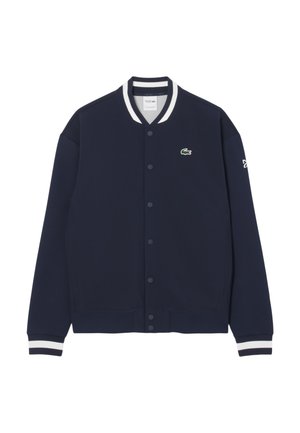Chaqueta de mezcla de algodón azul marino con cuello y puños de canalé de rayas blancas, cierre frontal de botones y pequeño logo verde en el pecho.