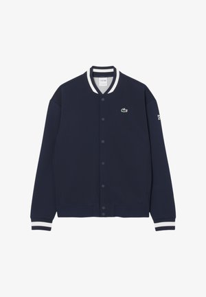 Chaqueta de mezcla de algodón azul marino con cuello y puños de canalé de rayas blancas, cierre frontal de botones y pequeño logo verde en el pecho.