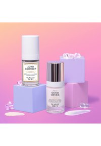 Deux bouteilles de soins de la peau : une bouteille blanche et une bouteille argentée étiquetées "AUTO CORRECT" et "GOOD GENES", placées sur des cubes de couleur pastel avec des accents nacrés.