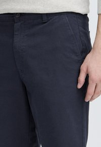 Pantalons en coton bleu marine avec une texture lisse, coupe droite et poches latérales. Comprend une fermeture à glissière et un bouton unique.