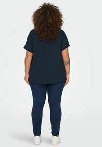 Marineblå kortermet topp med rundet kant, paret med mørkeblå skinny jeans og hvite joggesko; har myk stoff og avslappet passform.