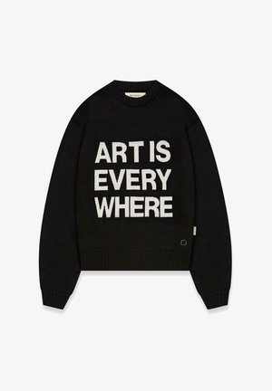 Zwarte gebreide trui met geribbelde manchetten en zoom. Heeft witte tekst met "KUNST IS OVERAL" prominent op de voorkant.