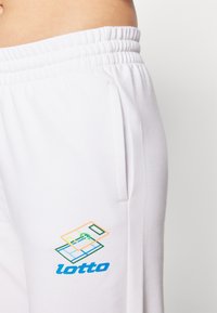 Baltie kokvilnas joggeri ar elastīgu jostasvietu, ar sānu kabatām. Izcils zils un daudzkrāsains "lotto" logo kreisajā augšstilbā.