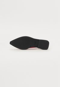 Scarpa nera a punta con suola texturizzata, caratterizzata da un accento rosso sul tacco. Il design è elegante e allungato, realizzato in materiale liscio.