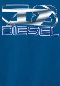 Blå bomull t-skjorte med et fremtredende hvitt og blått stripete grafisk design med teksten "DIESEL" i fete bokstaver.