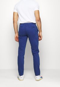 Blå, slim-fit bukser med baglommer og let stræk; båret med en hvid t-shirt med rund hals og hvide sneakers.