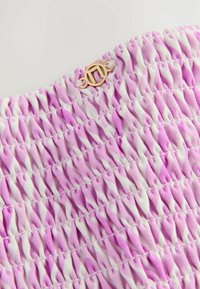 Tessuto smockato rosa e bianco con un motivo a onde texturato, caratterizzato da un piccolo logo metallico dorato. Materiale morbido e colore vivace.