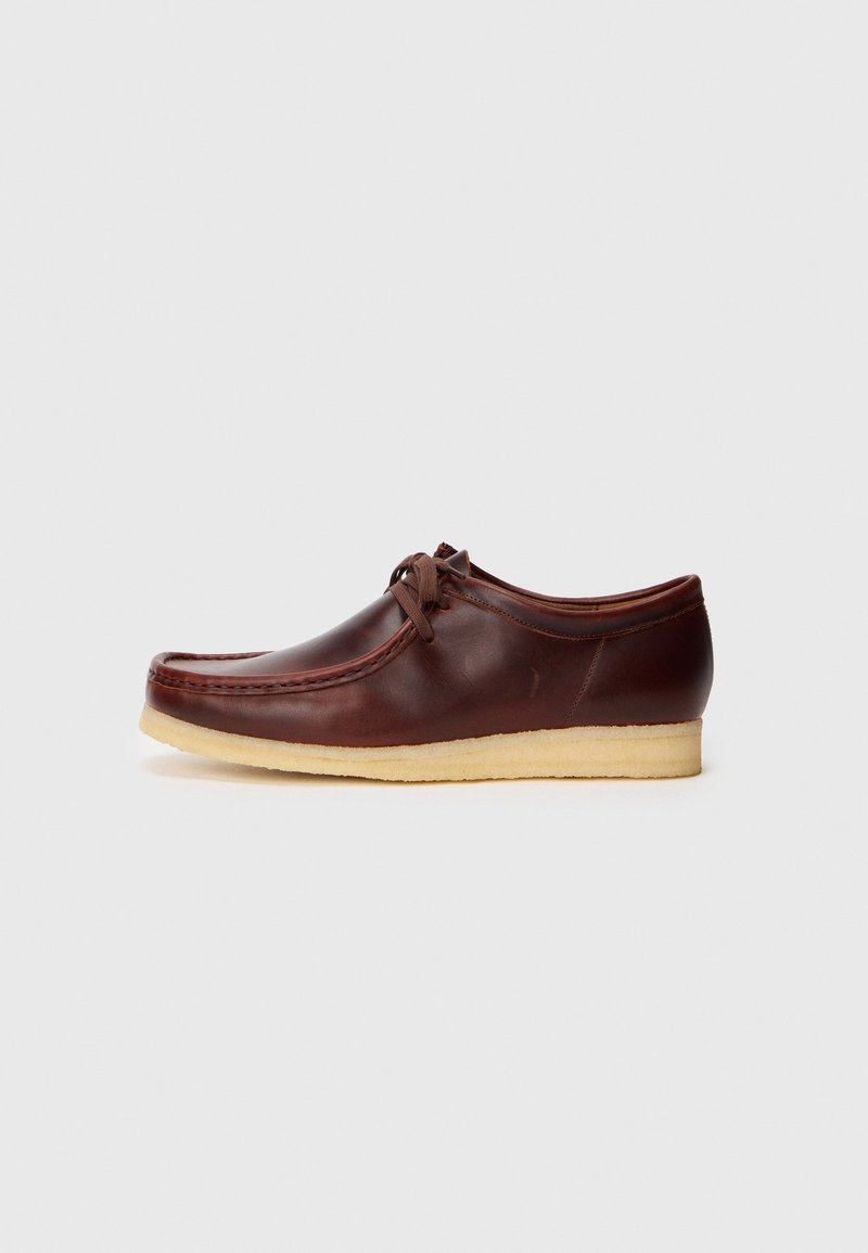 Zapato de mocasín de cuero marrón con suela de crepe y cordones, mostrado de lado sobre un fondo claro y liso.