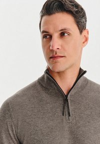 Szary sweter rozpinany wykonany z miękkiego materiału, z wysokim kołnierzem i minimalistycznym designem. Zamek błyskawiczny przy dekolcie, gładka faktura.