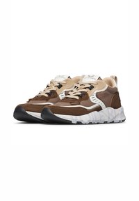 Un paio di sneakers marroni, beige e bianche con suole bianche spesse e lacci beige, esposti affianco su uno sfondo bianco.