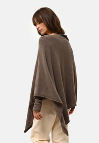 Brązowy wełniany ponczo o szerokim, drapowanym kroju, z długimi rękawami i subtelną fakturą. Posiada złożony kołnierz oraz otwory na ręce dla dodatkowego ciepła.