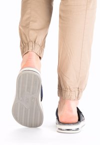 Sandale bleu marine avec une tige texturée, à enfiler, et une épaisse semelle blanche avec un dessous en caoutchouc gris contourné. Pantalons en tissu léger.