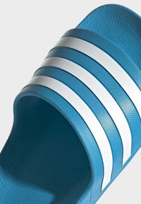 Blauwe slide sandaal met een reliëfoppervlak, voorzien van drie witte parallelle strepen op de band en een gladde zool.