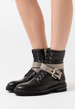 Black leather ankle boots with a textured silver strap and buckle detail, featuring gold hardware, round toe, and rugged sole.