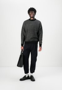 Maglione a strisce bianche e nere, pantaloni navy a vestibilità ampia, scarpe nere, calzini bianchi e una borsa a tracolla in pelle nera. Outfit casual su un modello.