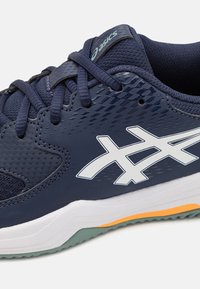 Zapatilla atlética de la marina con tejido de malla texturizado y parte superior sintética, acentos blancos, cuello acolchado y suela de goma con detalles en naranja y verde.