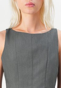 Grå ärmlös klänning med en figurnära bodice, med vertikala sömmar och en rak halsringning. Slät textur, minimal detaljering.