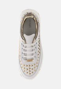 Sneakers bianche con borchie dorate, dettagli metallici e lacci grigi. Presentano una tomaia texturizzata e una suola imbottita per il comfort. Logo del marchio visibile.