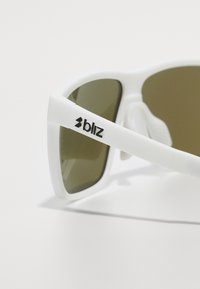 Occhiali da sole bianchi con lenti verde oliva, caratterizzati da una montatura spessa e un logo laterale nero. Testura liscia, design geometrico moderno.