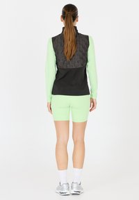 Gilet senza maniche nero e grigio sopra una maglietta a maniche lunghe verde menta, abbinato a pantaloni corti aderenti verde menta e scarpe da ginnastica argentate.